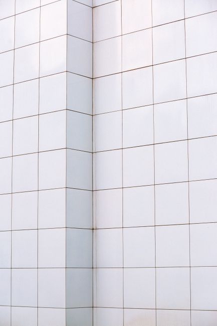 Close-up of a person wearing blue disposable gloves and a white protective suit using a blue cloth to clean and restore the grout lines between white ceramic bathroom tiles on a sink or bathtub edge,